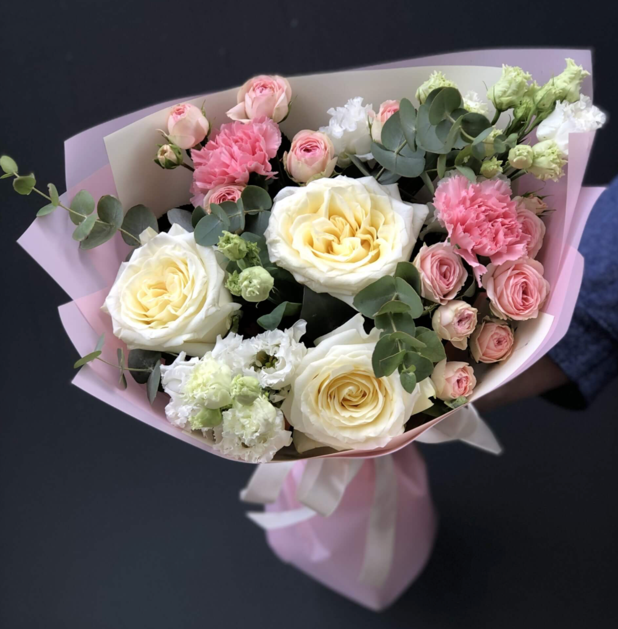 Ein Strauß aus Rosen, Eustoma, Nelken und Eukalyptus in Verpackung